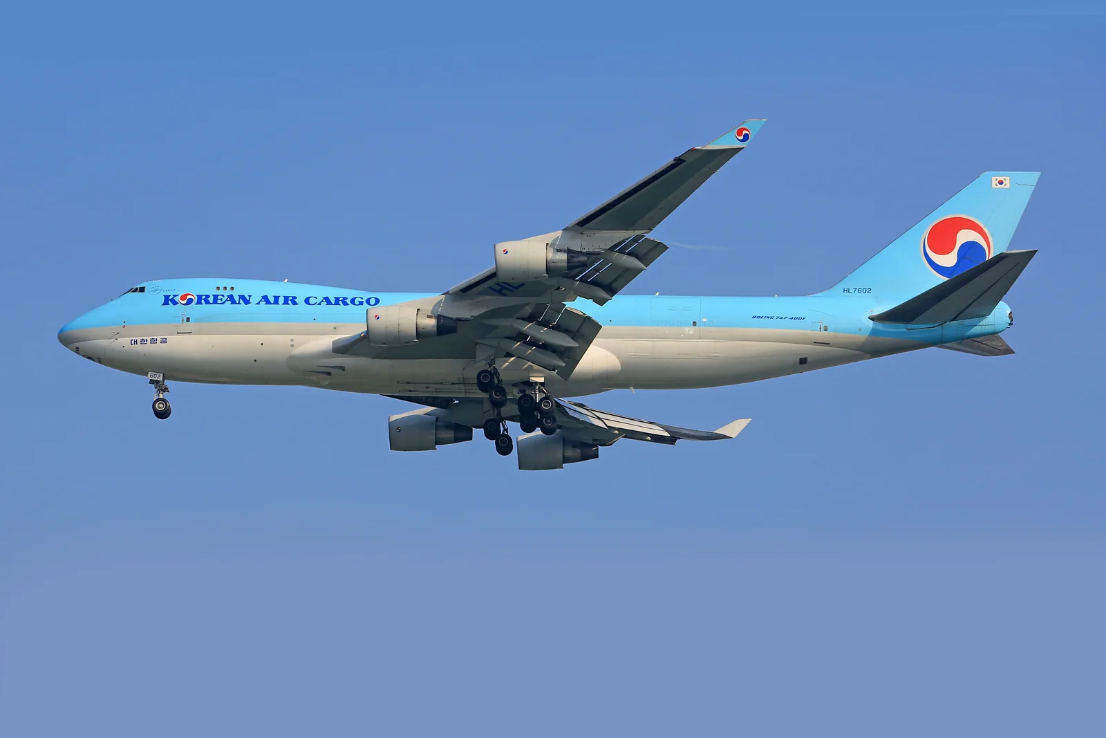 A white and blue cargo aircraft flying through a clear sky.