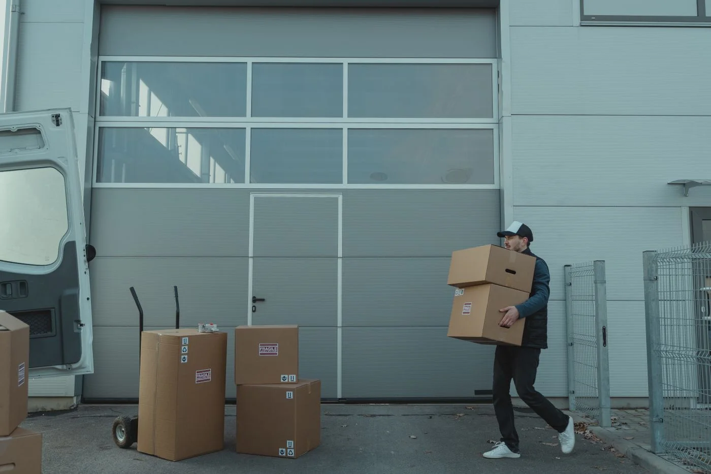 A courier carrying cardboard parcels outside a warehouse.